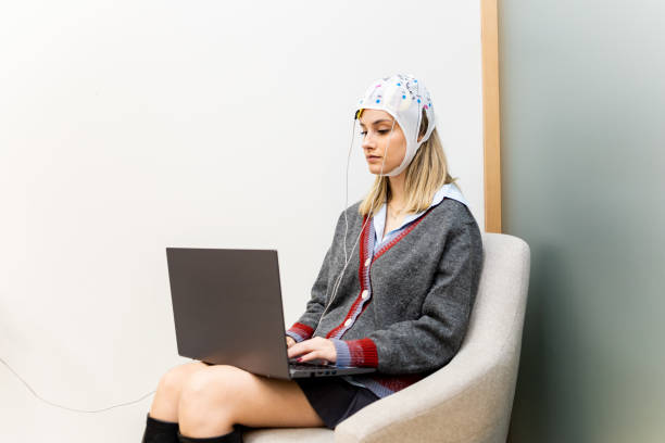 A pretty girl is sitting in a psychology office while interacting with a laptop and undergoing transcranial direct current stimulation. TDCS concept A pretty girl is sitting in a psychology office while interacting with a laptop and undergoing transcranial direct current stimulation. TDCS concept tDCS stock pictures, royalty-free photos & images