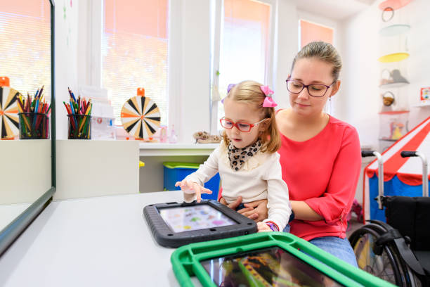 Non-verbal girl living with cerebral palsy, learning to use digital tablet device to communicate. People who have difficulty developing language or using speech use speech-generating devices. Non-verbal girl living with cerebral palsy, learning to use digital tablet device to communicate. People who have difficulty developing language or using speech use speech-generating devices. communication tablet stock pictures, royalty-free photos & images